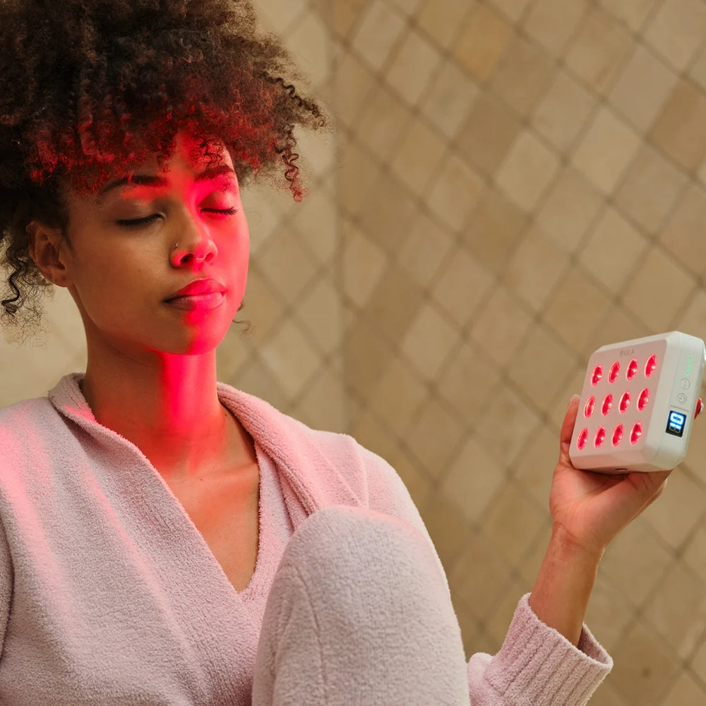 Woman holding the Kala Red Light Mini 2.0 device in a bathroom setting