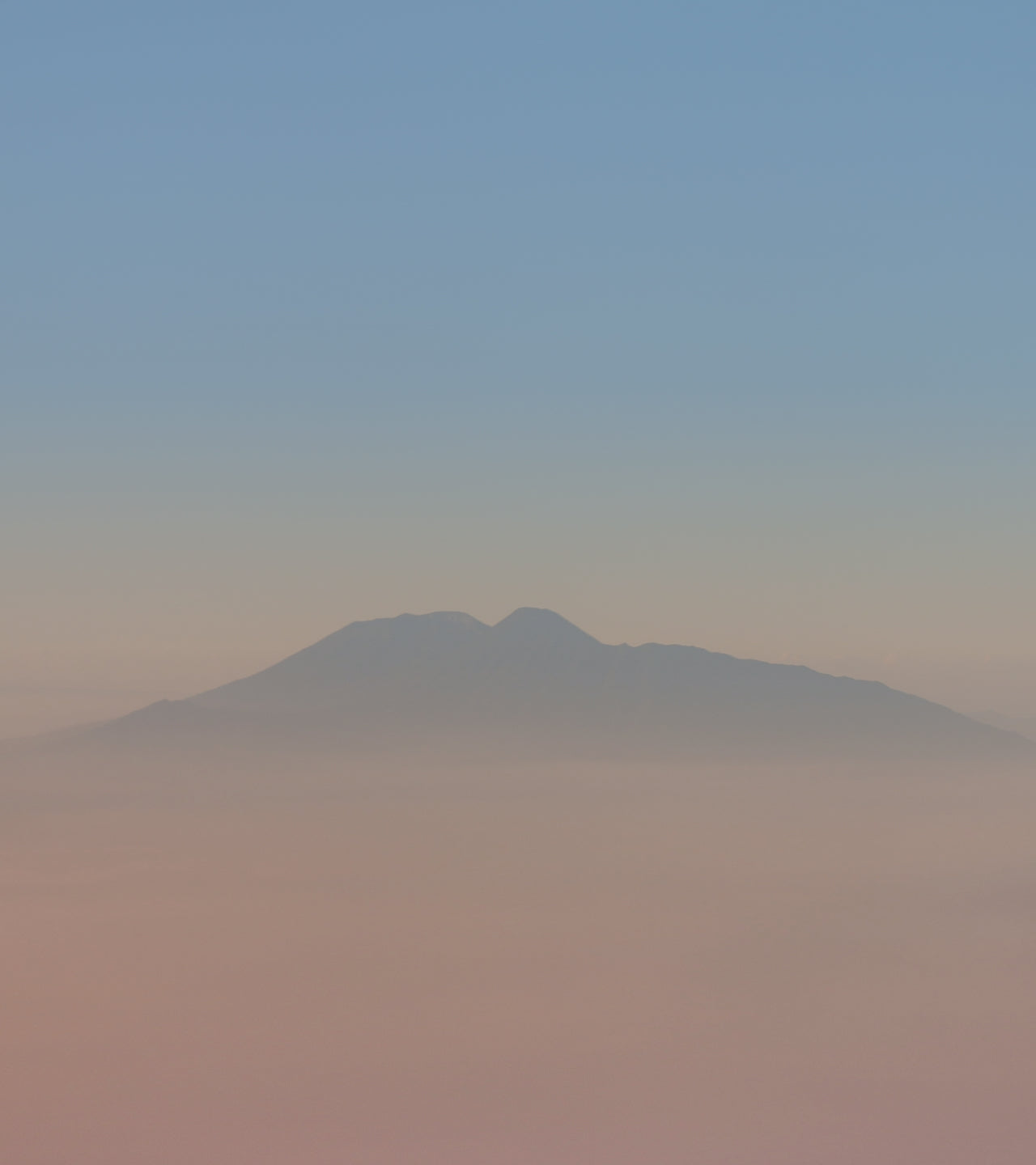 Mountain peak shrouded in mist with a gradient sky transitioning from blue to pink