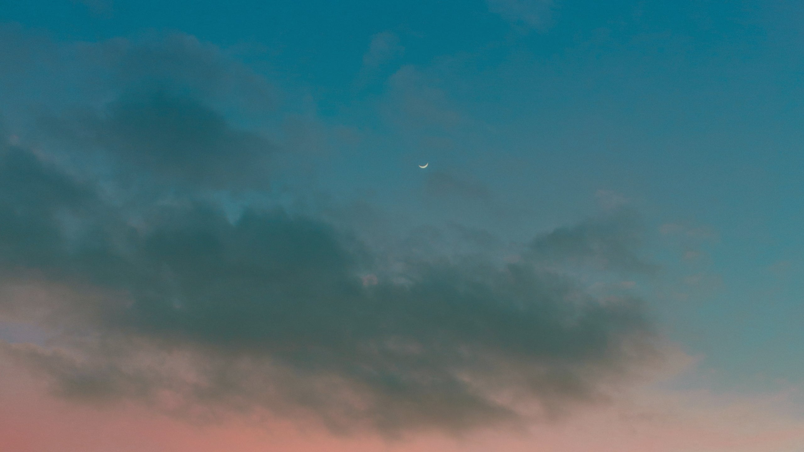 Small crescent moon against a dark blue sky with some clouds and pink hues
