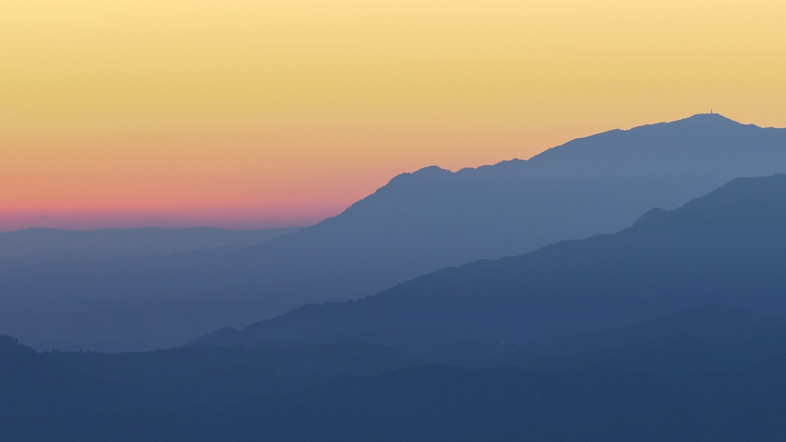 Silhouette of blue mountains against a colourful yellow, orange and pink sky during sunrise