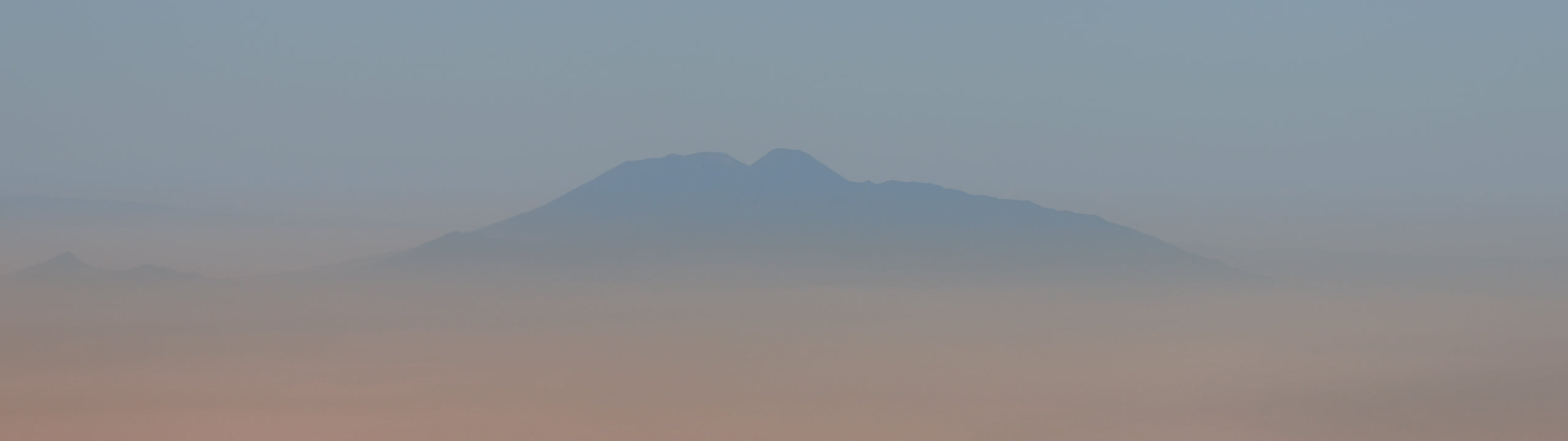 Hazy mountain range in a desert landscape with blue/grey and soft pink colours