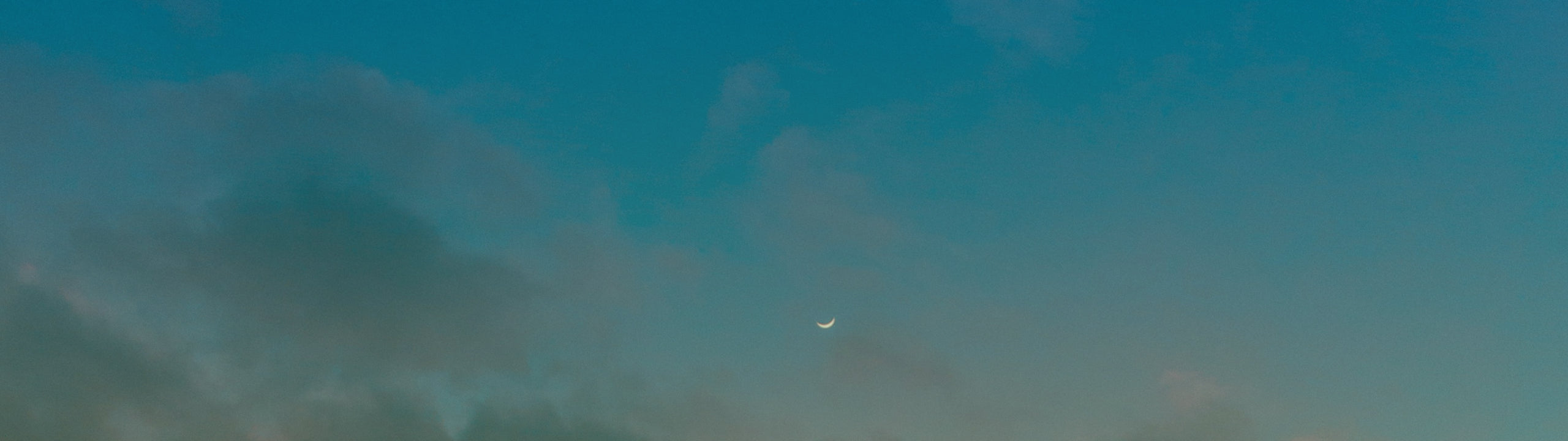 Small crescent moon against a dark blue sky with some clouds