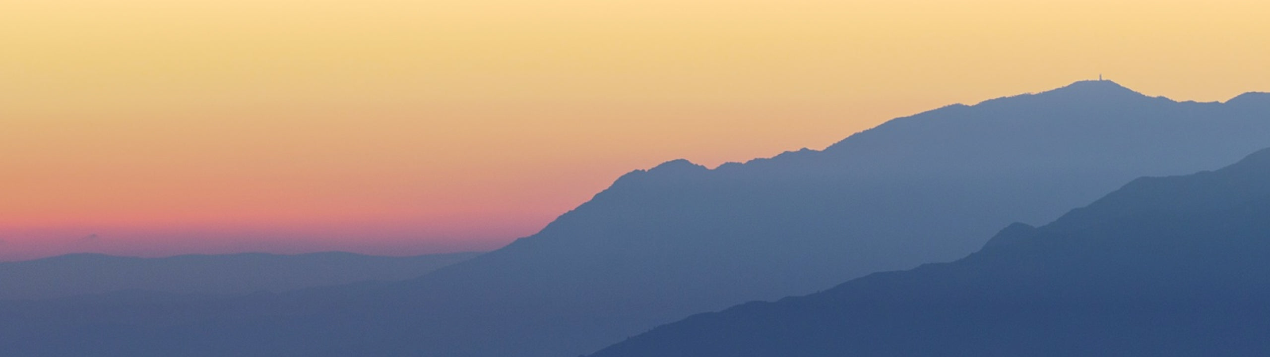 Silhouette of blue mountains against a sunrise sky with warm colours