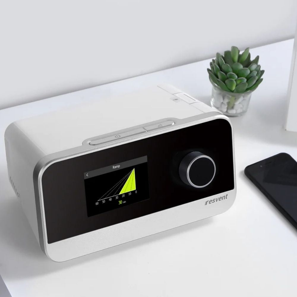 Resvent iBreeze Auto CPAP Machine on desk beside a succulent and phone