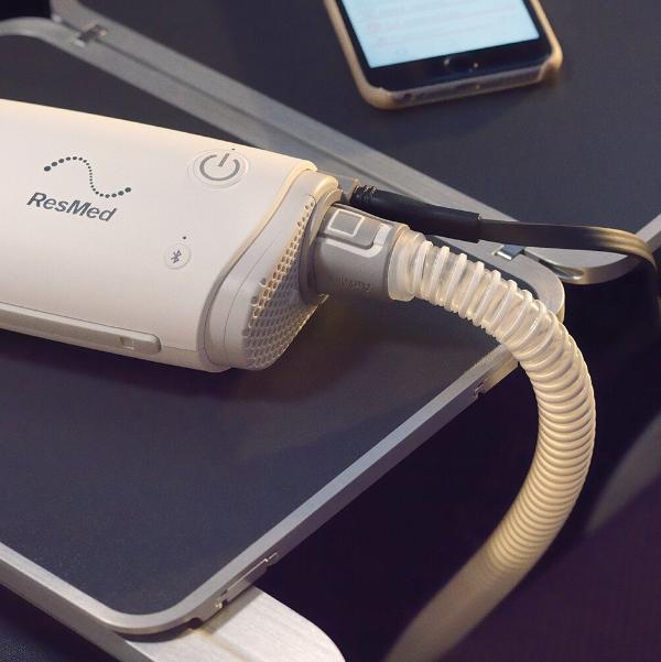 ResMed AirMini Charger shown plugged into AirMini device on airplane tray table