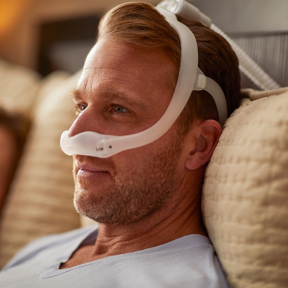 Man wearing the Philips DreamWear Nasal Mask while sitting up in bed