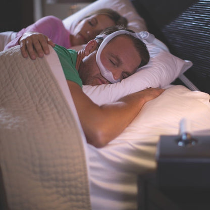 Two people sleeping in bed, one person using using the Philips DreamWear Nasal Mask while sleeping on their stomach
