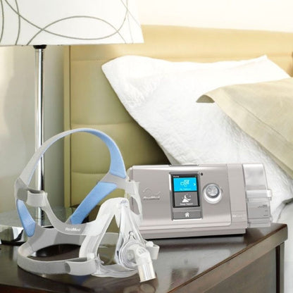 ResMed AirCurve 10 BiPAP machine and full face mask on a nightstand next to a bed