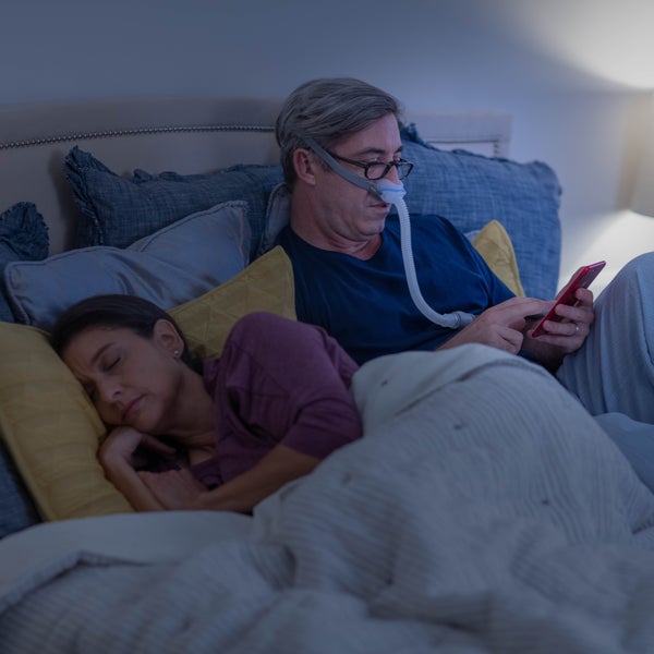 Person wearing glasses using the ResMed AirFit N30 nasal CPAP mask while in bed on his phone