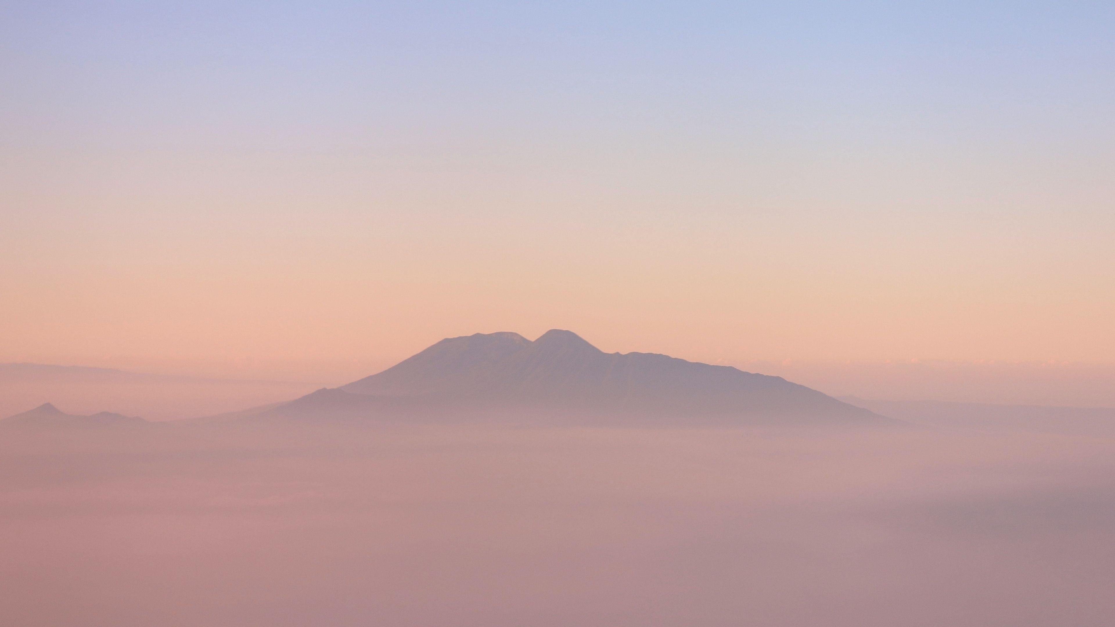 Mountain peak emerging from mist at sunrise with a soft pink and blue sky