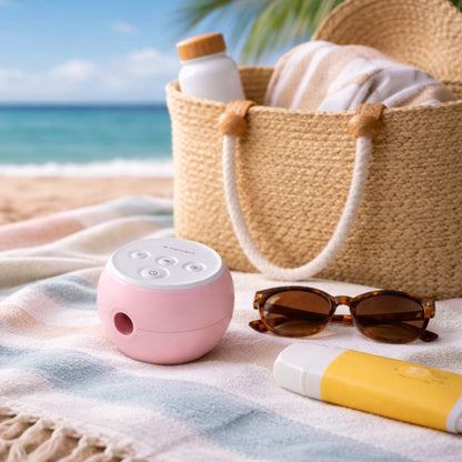Pink Transcend Micro 510 travel CPAP device on a towel with sunglasses and sunscreen, beach bag in the background